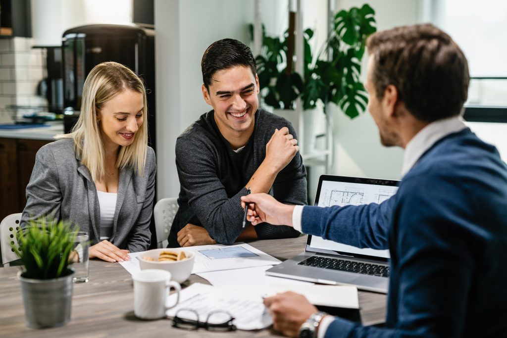 Young happy couple going through housing plans with real estate agent.